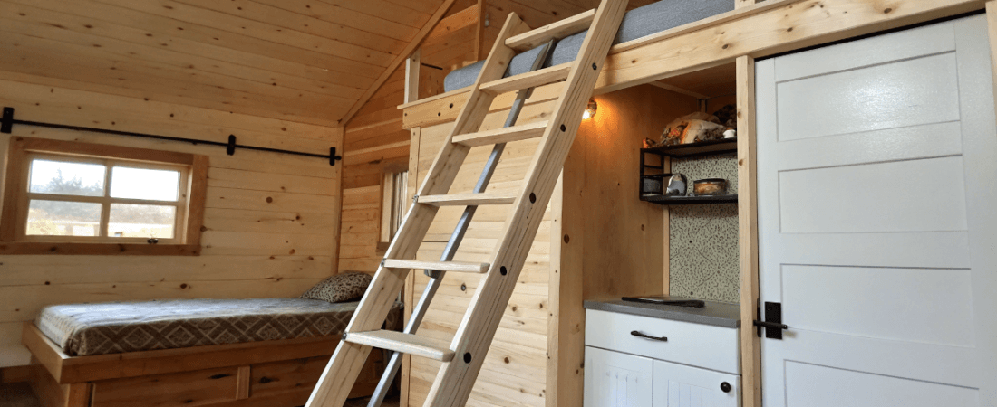 A cozy wooden bedroom with a rustic aesthetic The room features wooden walls a ladder leading to a loft area a simple brown toned mattress on a bed structure a white cabinet a white door a wooden ladder and a small window The overall design is warm and inviting with a focus on natural materials The image is a photo capturing the interior of the bedroom with natural lighting coming from the window The light wooden tones create a calm and comfortable ambiance