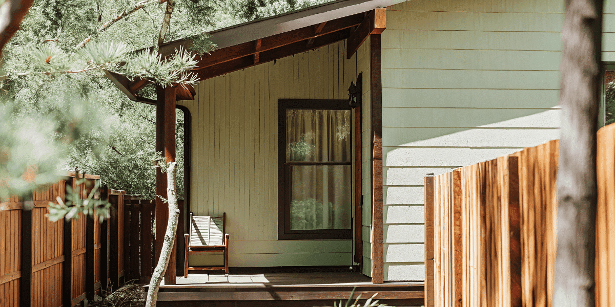 B1f80c56fa5a4cc2964992a84138813f A quaint rustic wooden and white cottage style house with a well maintained wooden fence and lush greenery