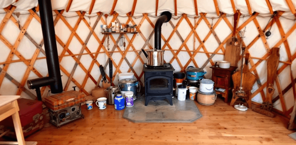 45bbd8f00bc24133945cb5771f6f19b2 An interior of a cozy yurt with wood stove pots pans cup