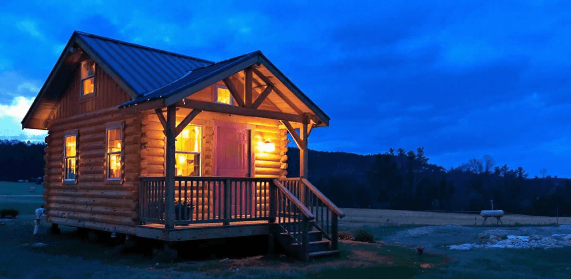 6389344d89a944849d2b1d279d22cc6a A photograph of a rustic cozy cabin style home during dusk The image captures the cabin's structure, with a prominent wooden exterior, featuring a combination of natural wood tones and a warm glow emanating from the windows.
