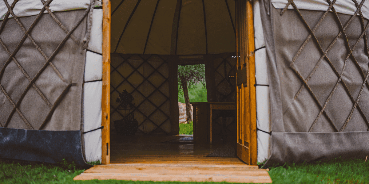B7ddab15dcc247d6aebb74cc480c654f A photo of a traditional Mongolian style tent known as a yurt situated outdoors with a view of the surrounding greenery The yurt's entrance is visible, with its characteristic wooden framework and intricate weaving of the exterior.
