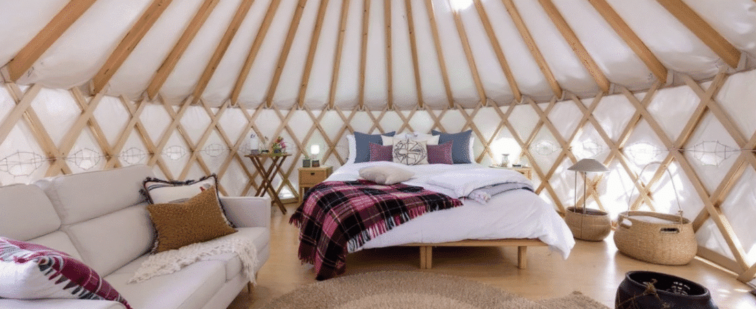 A photograph of a cozy traditional style interior of a well lit and inviting space within a wooden walled tent like structure known as a yurt