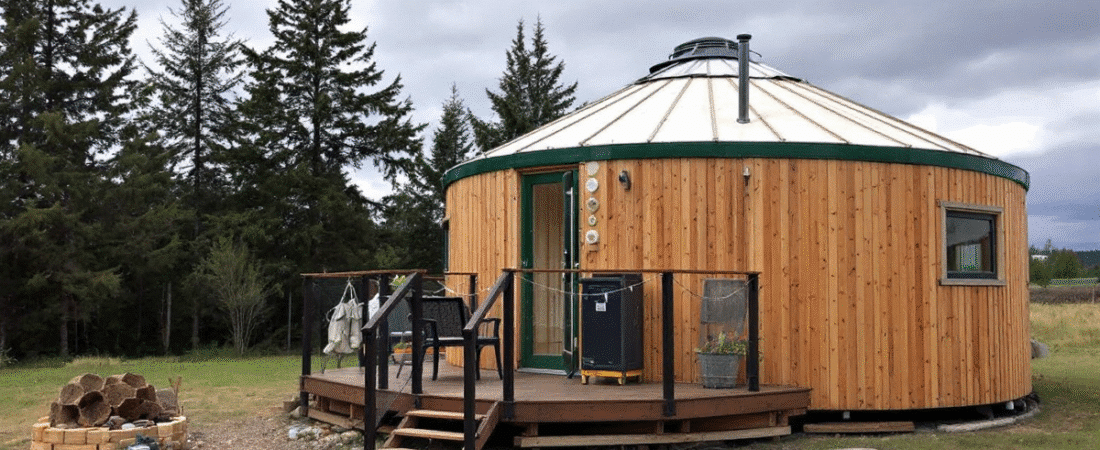 A photo of an outdoor scene with a focus on a rustic wooden structure resembling a traditional yurt with a distinctive curved dome shaped roof