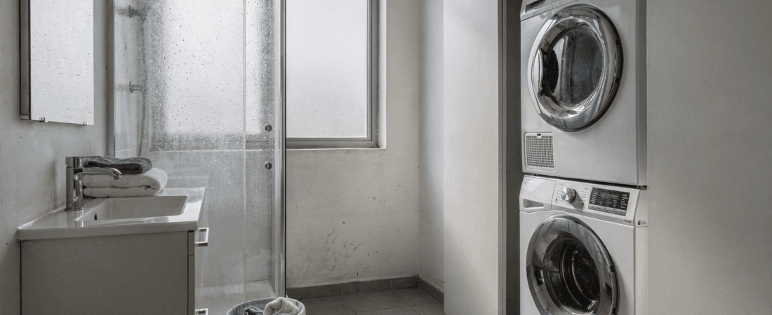 Laundry bathroom combo A laundry room with a washing machine and dryer stacked next to a sink with towels and a glass shower