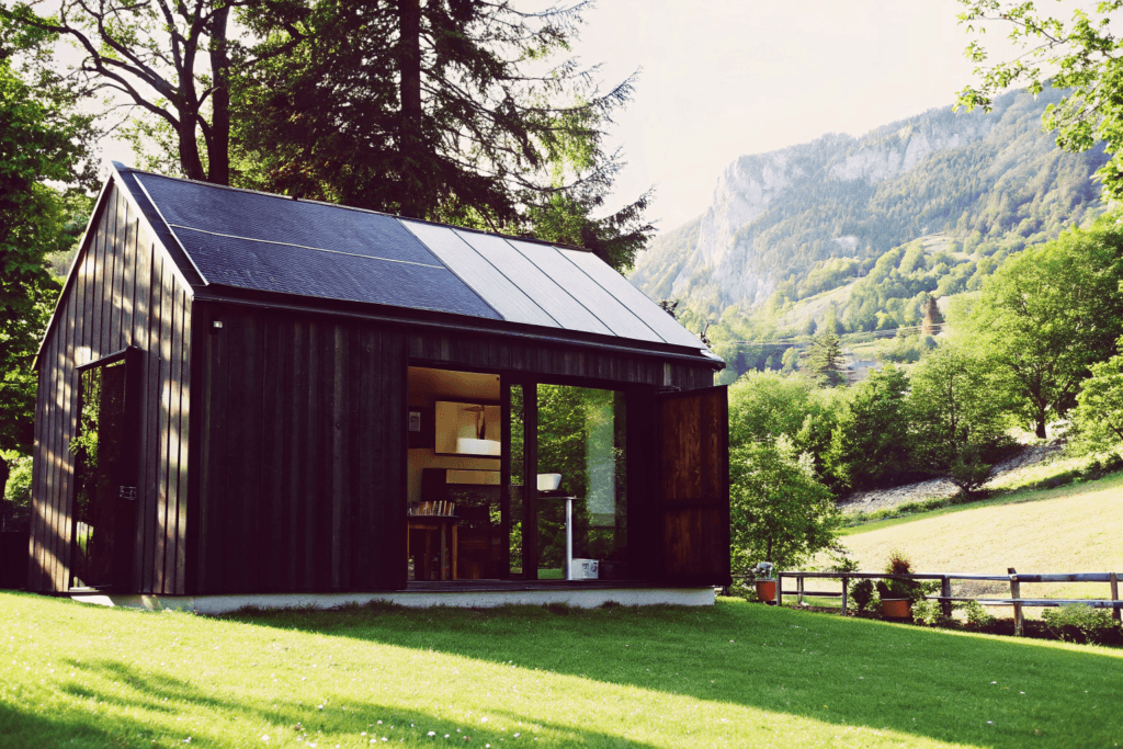 Expandable accordion Photograph of a modern sustainable tiny home with solar panels in a picturesque mountain meadow depicting a family enjoying remote work relaxation and play in nature