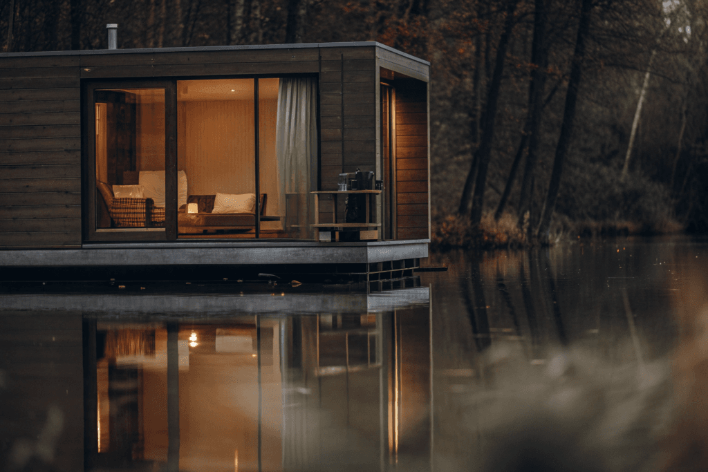 Floating studio Show the full house A realism realistic HDR photograph taken with a DSLR camera camera quality photo of a Photograph of a modern sustainable floating cabin on a serene lake surrounded by a lush forest with a woman working peacefully on its deck