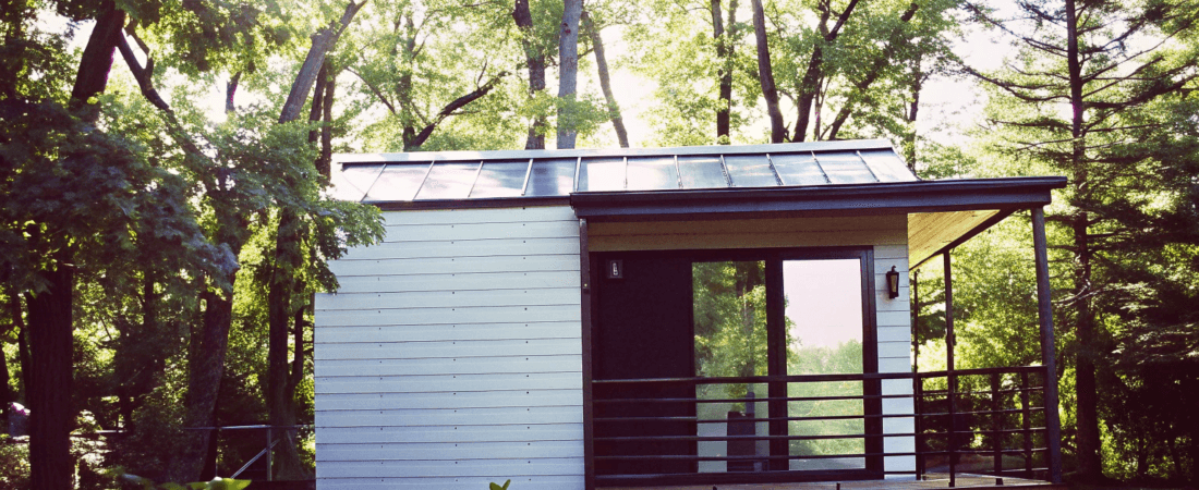 Modern tiny house Photograph of a modern minimalist tiny house with solar panels and a wooden deck nestled in a lush sun dappled forest evoking tranquility and sustainable living