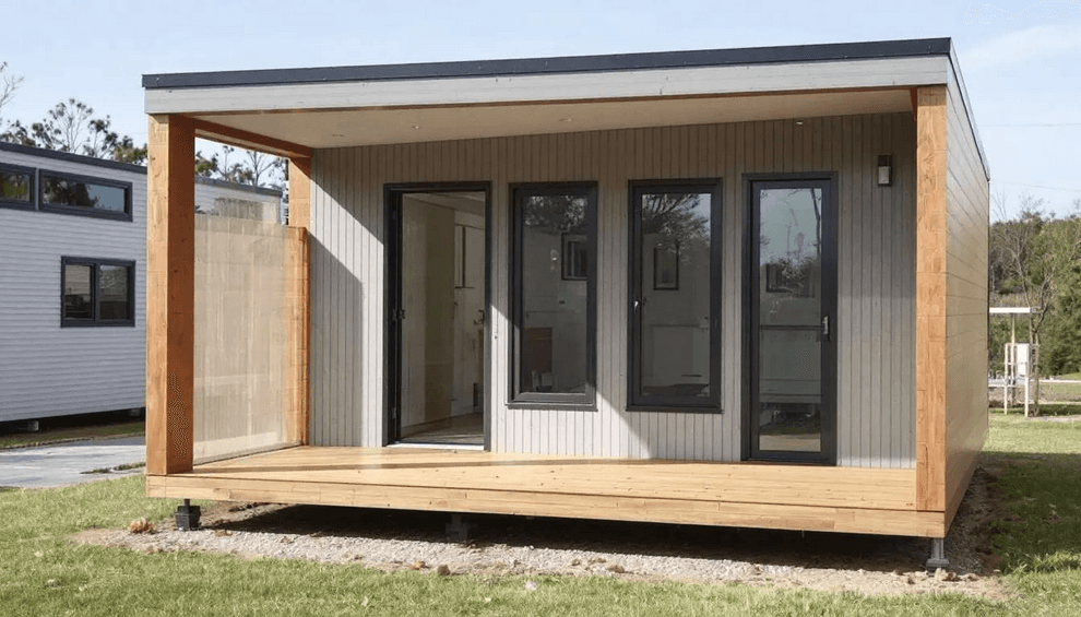 An exterior view of a charming two bedroom portable cabin showcases a warm and inviting atmosphere featuring natural cedar accents and a spacious front porch The modern design includes a high barn style roof enhancing its appeal as a cute little guest house perfect for family gatherings