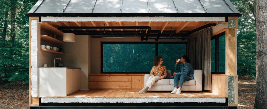 Noise insulated tiny home A cutaway photograph of a modern tiny home in a forest setting showcasing high quality construction materials like insulation and acoustic glass while a couple relaxes inside on a sofa