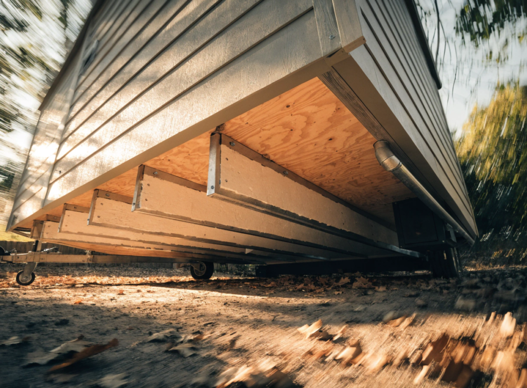 Floor Underside view of a large metal walled container on wheels parked on dirt with fallen leaves outdoors