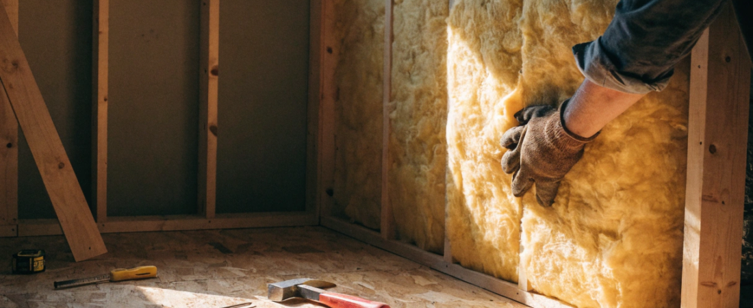 Mid construction Person wearing gloves presses yellow fiberglass insulation into a wooden stud wall during construction tools lie on the plywood floor nearby