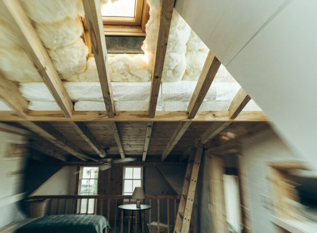 Roof insulation Attic bedroom under renovation with exposed wooden beams insulation a bed window and a ladder